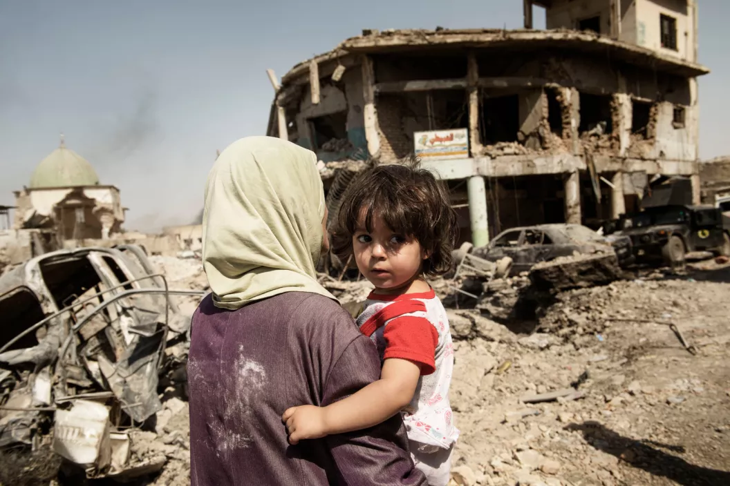 Iraq. A woman carries her child through the debris of buildings and vehicles destroyed during intense fighting