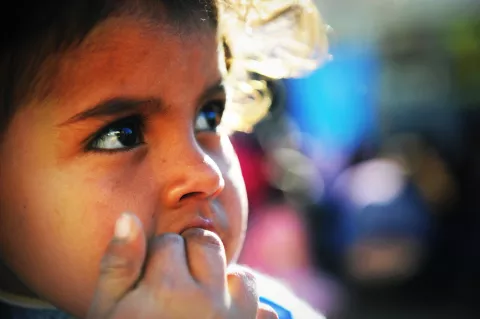 Una niña mira hacia la derecha, mientras se pone un dedo en la boca.