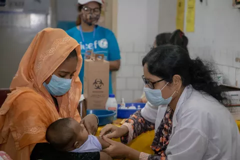 Volunteers help a Health Worker deliver a vitamin A capsule to Hamim, six-month-old, on 20 June 2021 at vaccination centre, (Radda MCH-FP Centre), Mirpur, Dhaka.