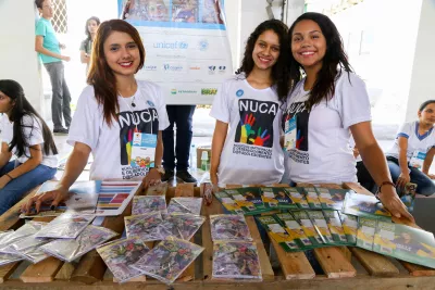 Três adolescentes participantes de projeto do UNICEF no Semiárido estão em pé atrás de uma mesa com publicações e folhetos