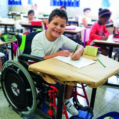 menino sorridente na sala de aula, ele usa cadeira de rodas