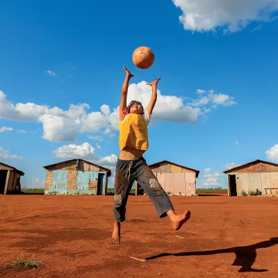 Foto mostra um menino saltando para pegar uma bola