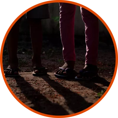Foto mostra os pés de duas crianças. A foto está escura.