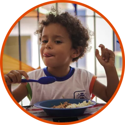 Foto mostra um menino pequeno comendo a merenda escolar
