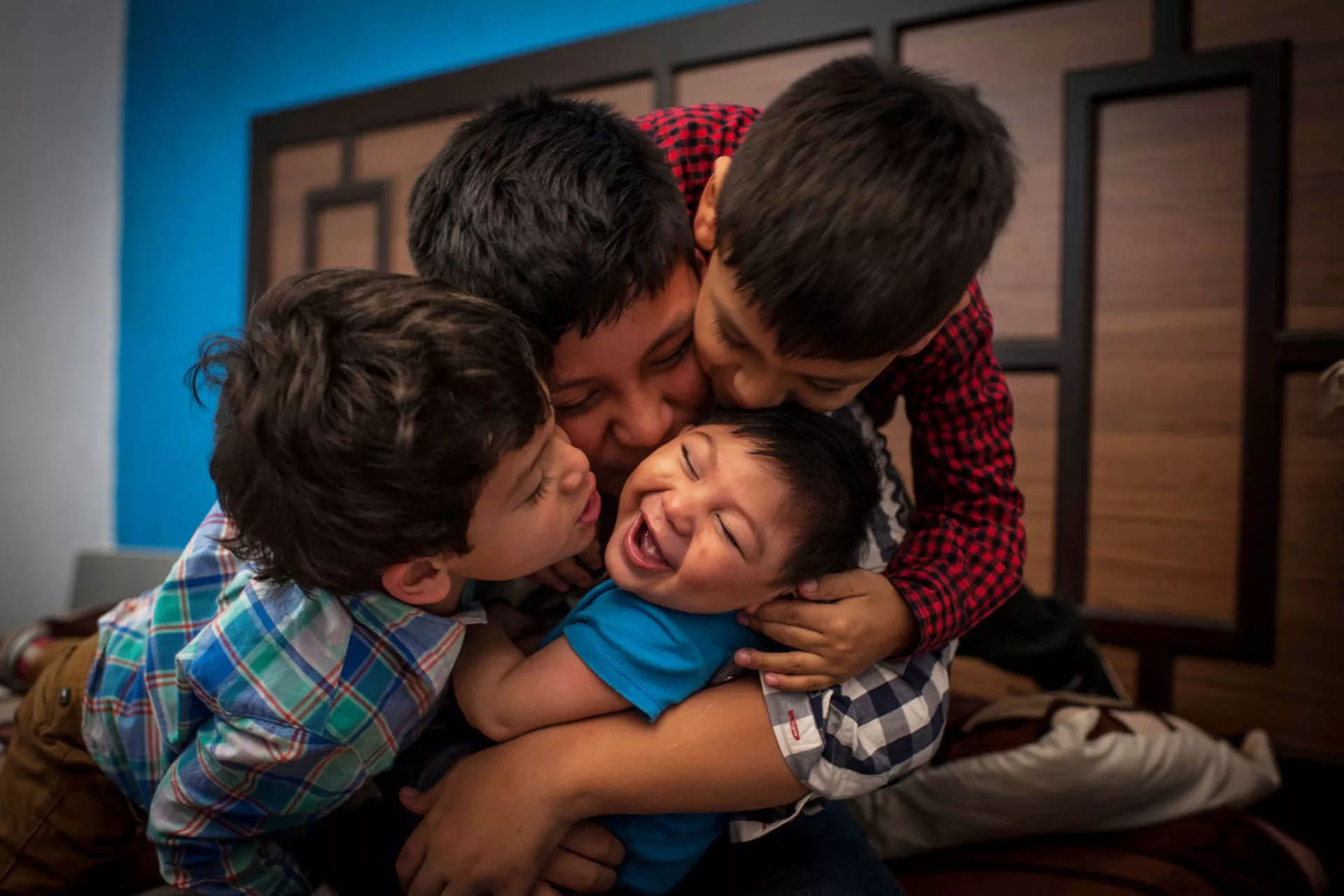 três meninos abraçam seu irmãozinho bebê, que está rindo