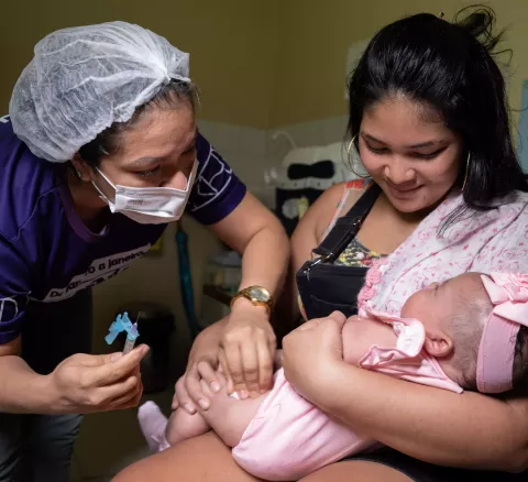 Profissional de Saúde aplica vacina em bebe no colo da mãe