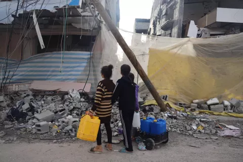 Foto mostra duas crianças de costas segurando galões de água
