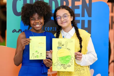 Foto mostra duas meninas segurando desenhos