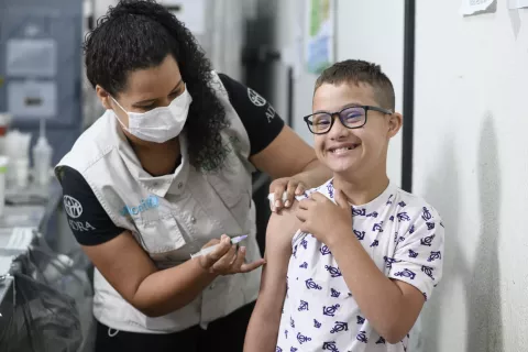 Técnica de enfermagem Angélica Morales aplica vacina no braço de uma criança com síndrome de down