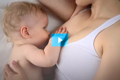 Foto extraída do vídeo mostra uma criança mamando no peito da mãe. A cabeça da mãe não aparece na foto.