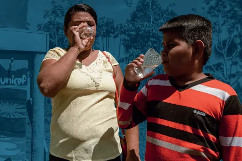 Foto mostra uma mulher e um menino ao lado de uma caixa d'água, bebendo água.