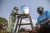 Na República Democrática do Congo, um menino pequeno lava as mãos em um torneira que sai de um filtro com o logo do UNICEF. Ao lado dele, um funcionário do UNICEF usando camiseta azul com a marca da organização. Os dois estão em espaço aberto.