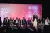 Foto mostra Thaynara OG, vestindo a camiseta do UNICEF, falando para uma plateia de pessoas. Ela está em pé em cima de um palco e atrás dela há outras pessoas sentadas.
