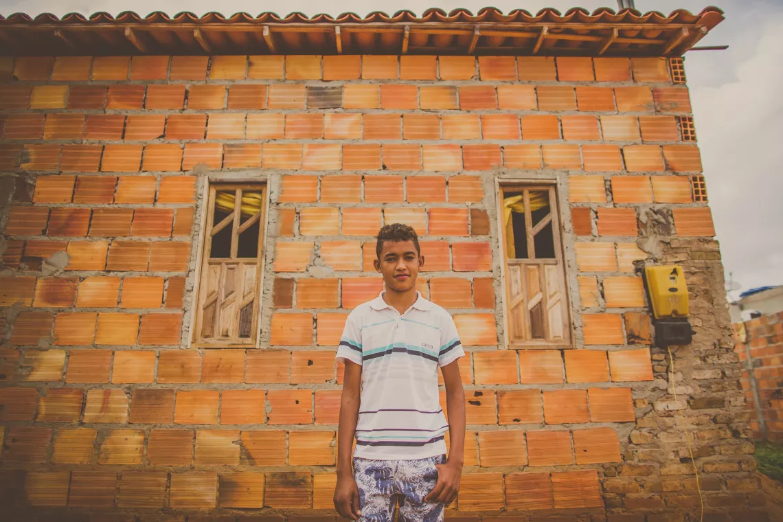 Adolescente está parado em frente a uma casa de tijolos aparentes.
