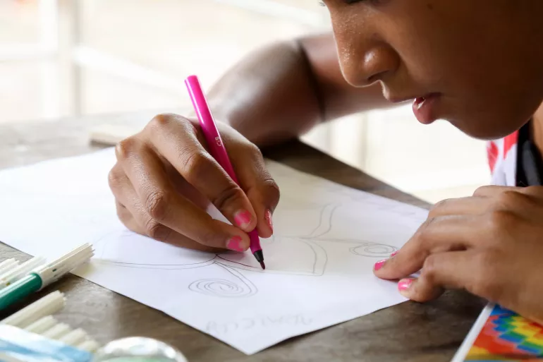 foto mostra rosto parcial de criança. ela está escrevendo em um papel