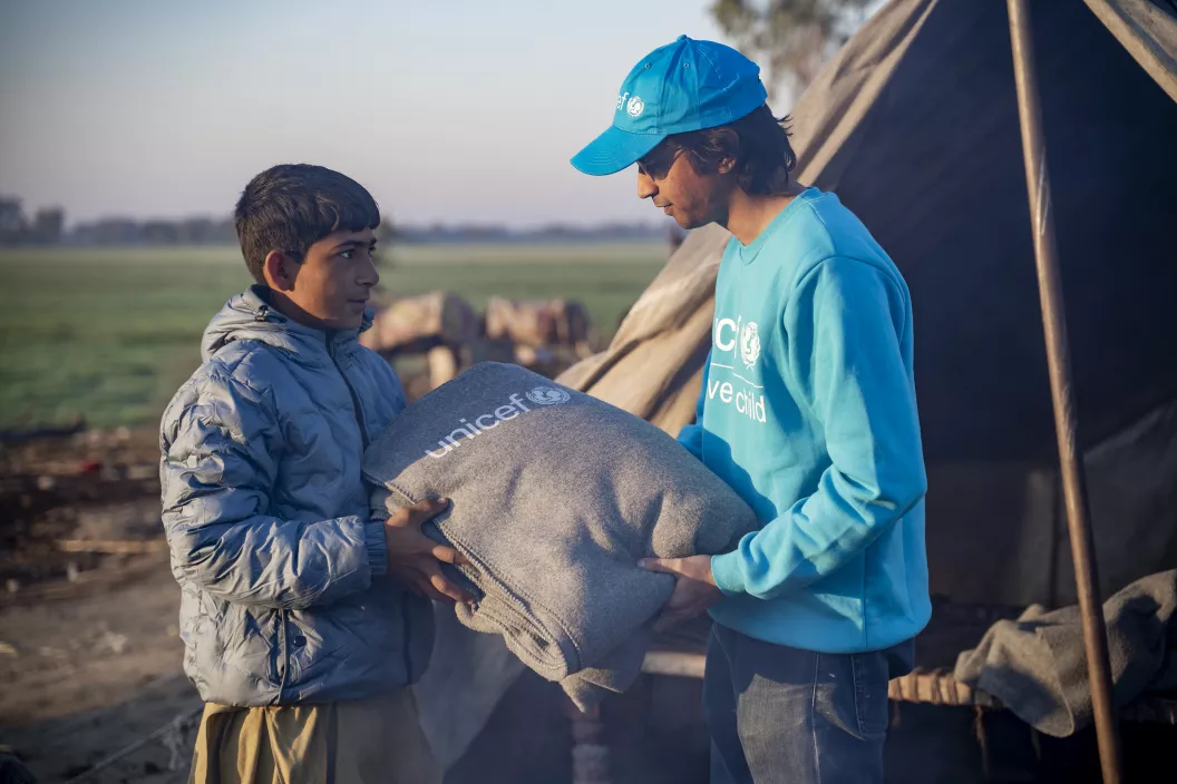 Um homem com roupa do UNICEF entrega um cobertor para um adolescente
