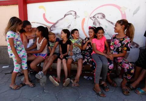 Деца от уязвими общности са седнали на пейка и се забавляват, зад тях има красиви графити
