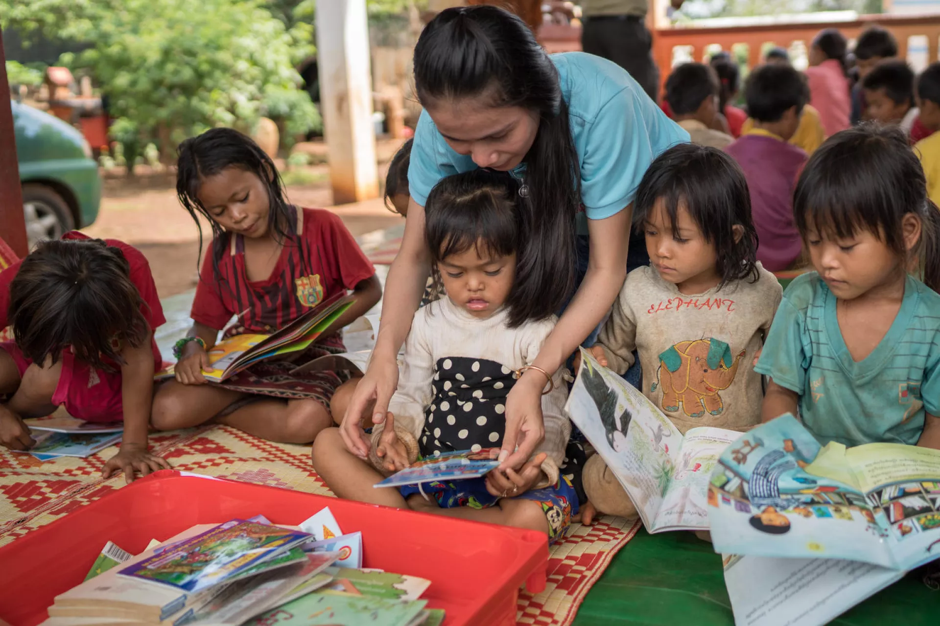 Sipar staff, Seun Sokhuan, assists children they read books in Kak Village, Kak commune, Borkeo Disctrict, Ratanakiri on June 13, 2018.