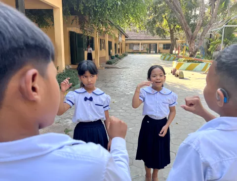 7-year-old student Duong Chay, a smiling girl with hearing impairment and autism, communicates with her classmates using sign language on the playground of Siem Reap Special Education High School. They excitedly discuss the games they will play when the school bell rings, signaling the start of their break. Photo credit UNICEF/Le Bun