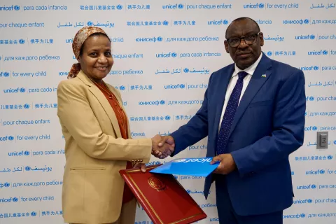 Woman and man shake hands holding a cyan blue folder that reads UNICEF