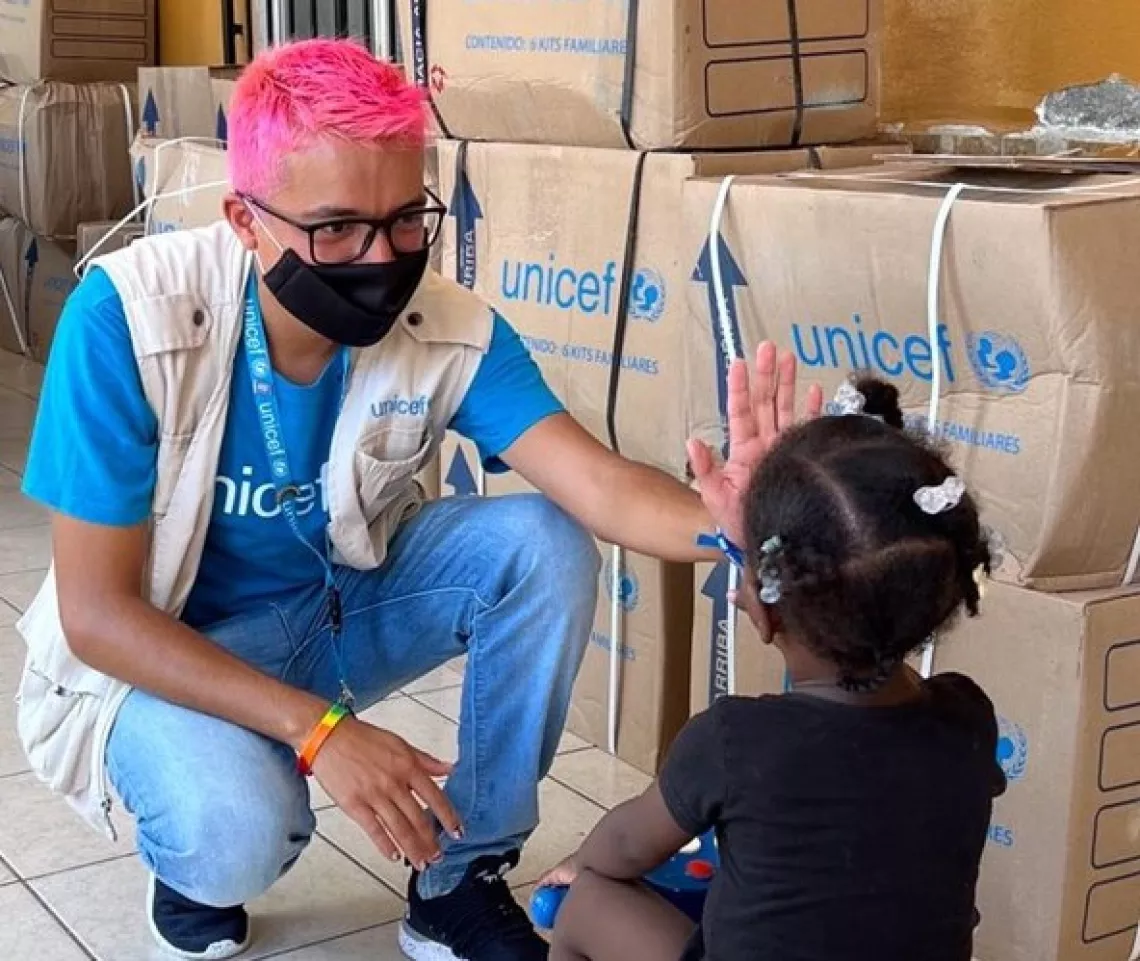 A young man gives high five to a child in fron of supply boxes that read UNICEF