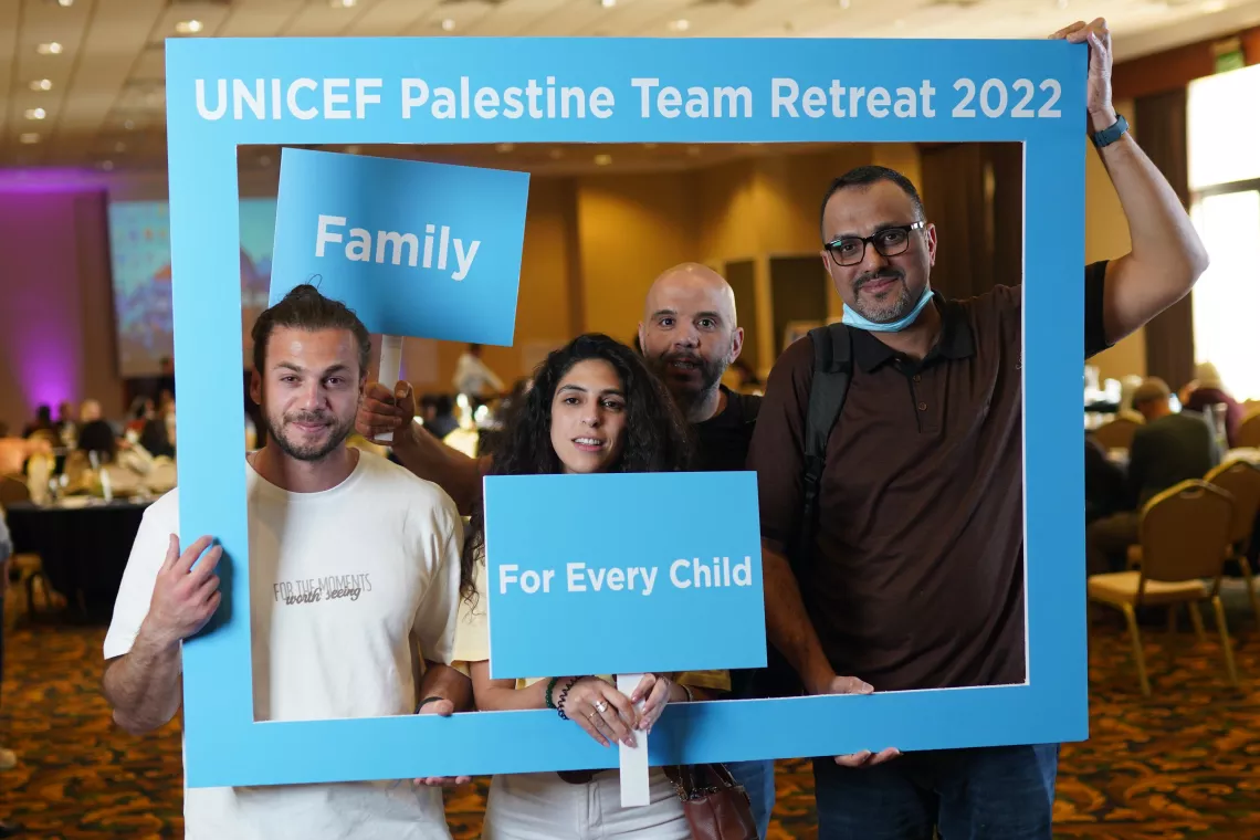 UNICEF employees smiling and standing behind a frame, holding signs that read "family" and "for every child"