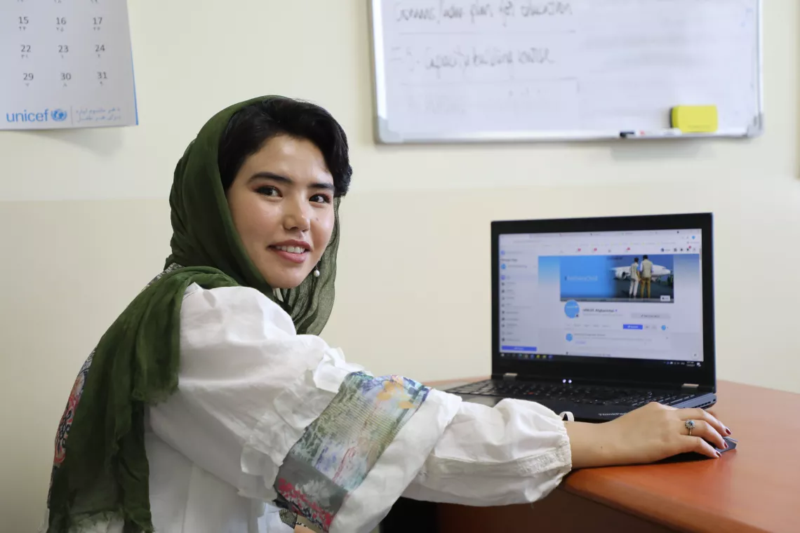 Girl sits in fron on her laptop and smiles in the UNICEF Afghanistan office