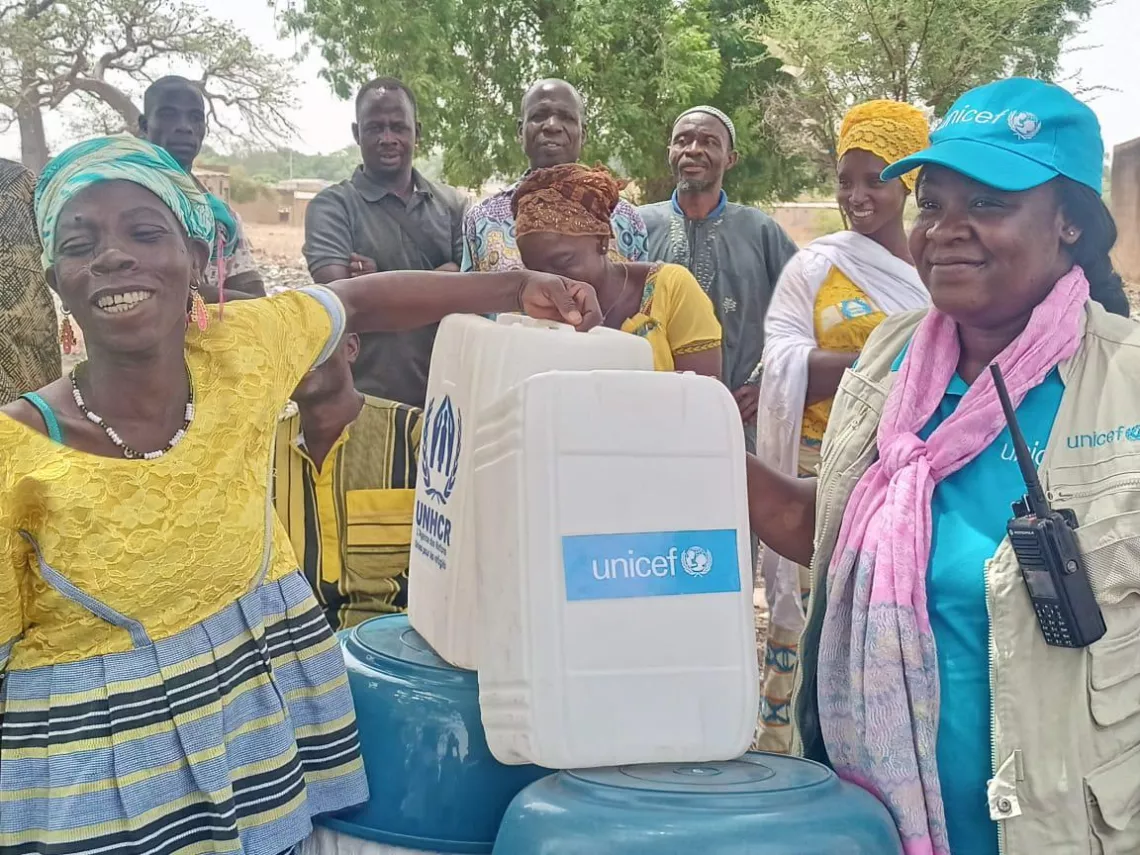 Woman wearing UNICEF branded cap and smiling engages with children and women