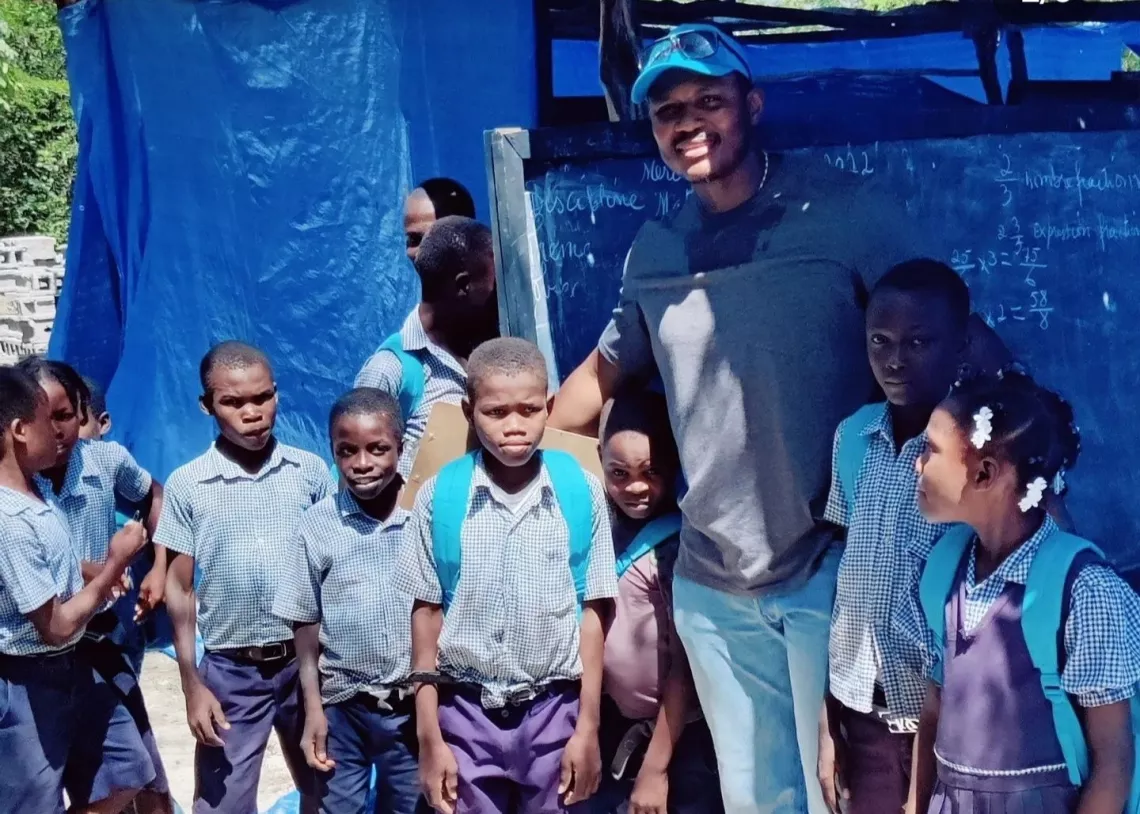 A man standing among children wearing backpacks in front of a school