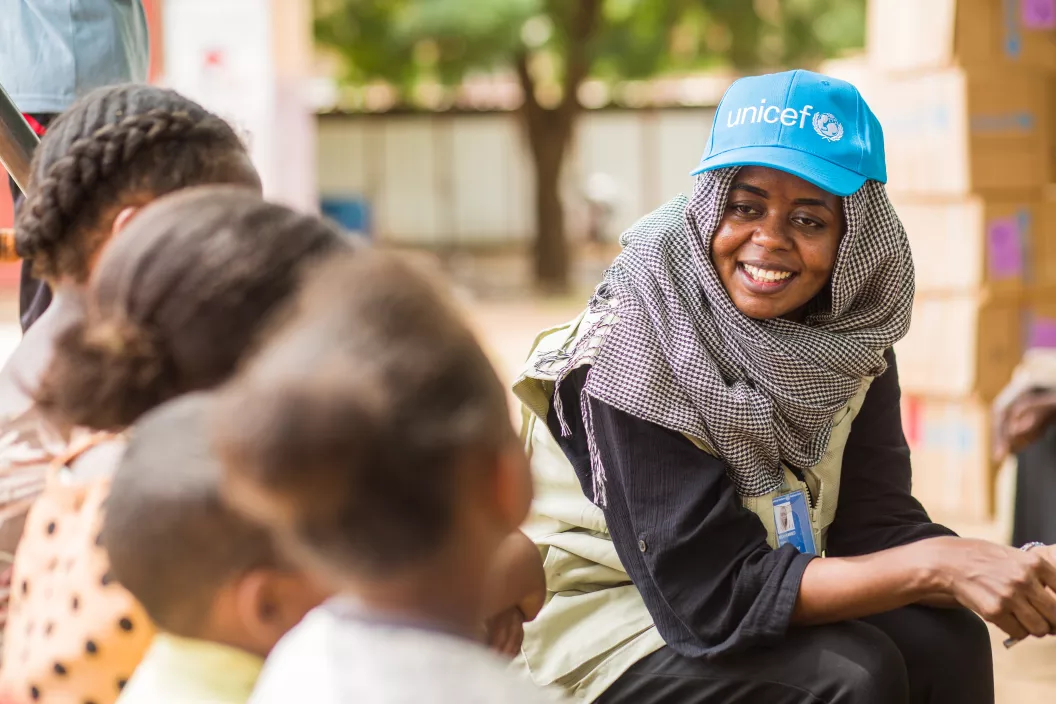 Woman wearing UNICEF branded cap and smiling engages with children