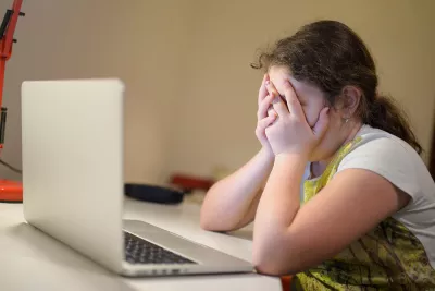 11-year-old Ajsa is photographed in front of a laptop, with her head in her hands.
