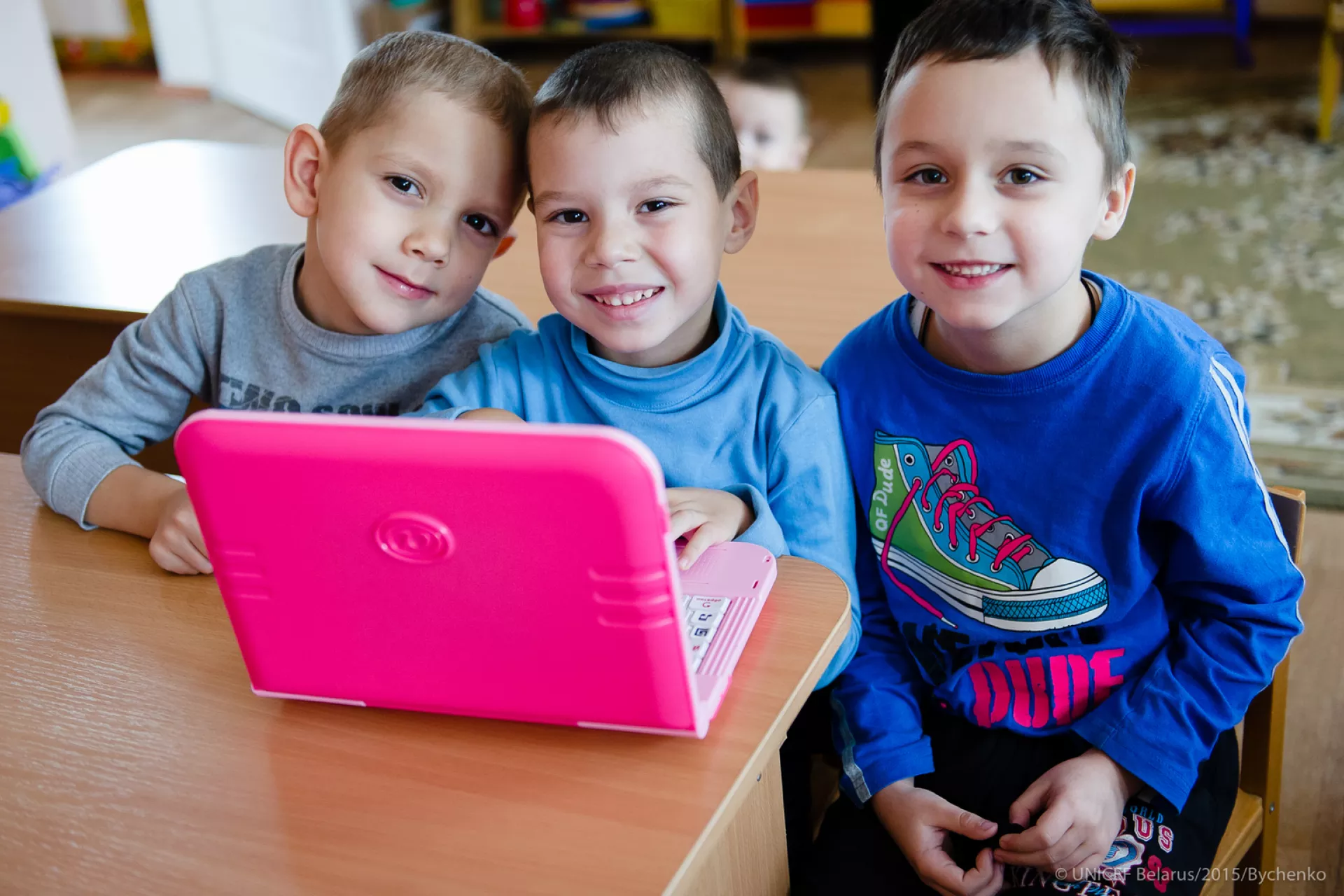 Three five-year-olds take part in a Kindergarten literacy and maths lesson on a small pink laptop.