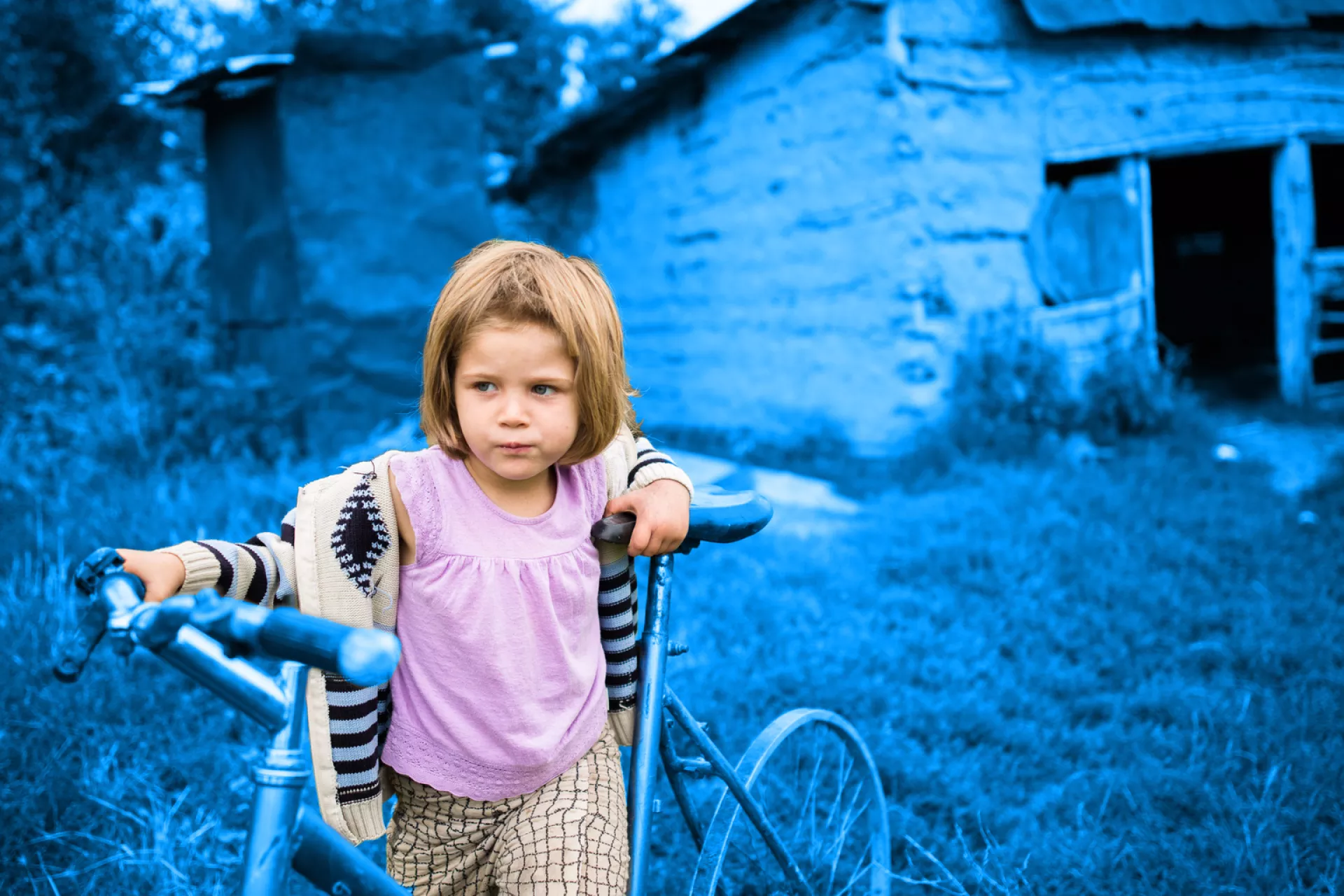 Four-year-old Flori Maria plays on a broken bike outside her family home in Romania.