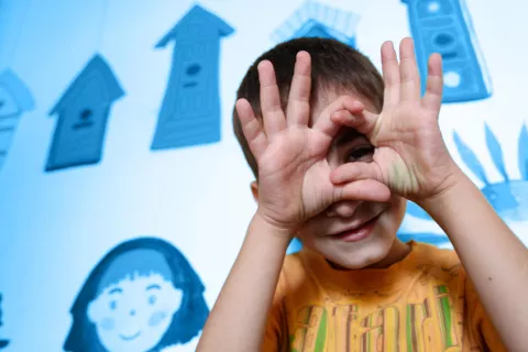 A child peers through his fingers towards the camera