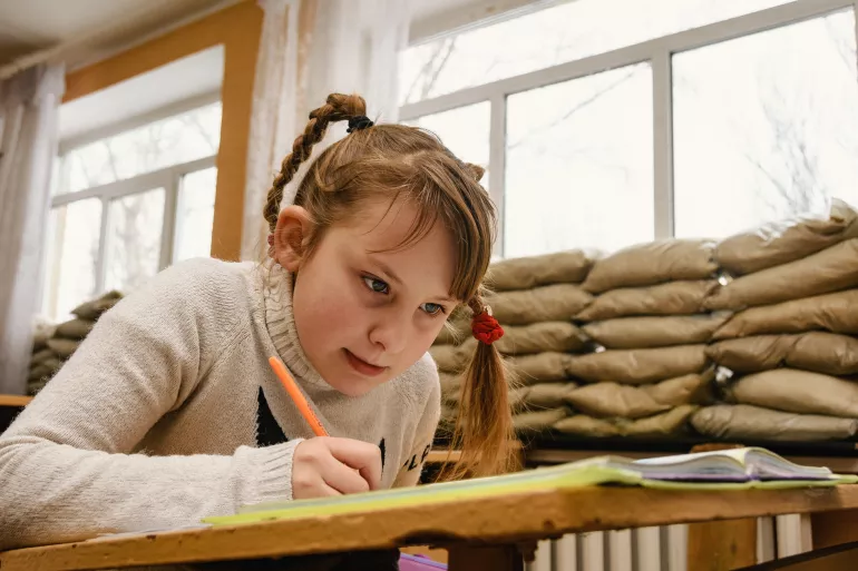 A young girl in a classroom in eastern Ukraine with windows blocked up with sandbags because of the frequent shelling.