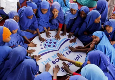 A group of young girls form a circle and place their hands on a sign for the Mogadishu book fair