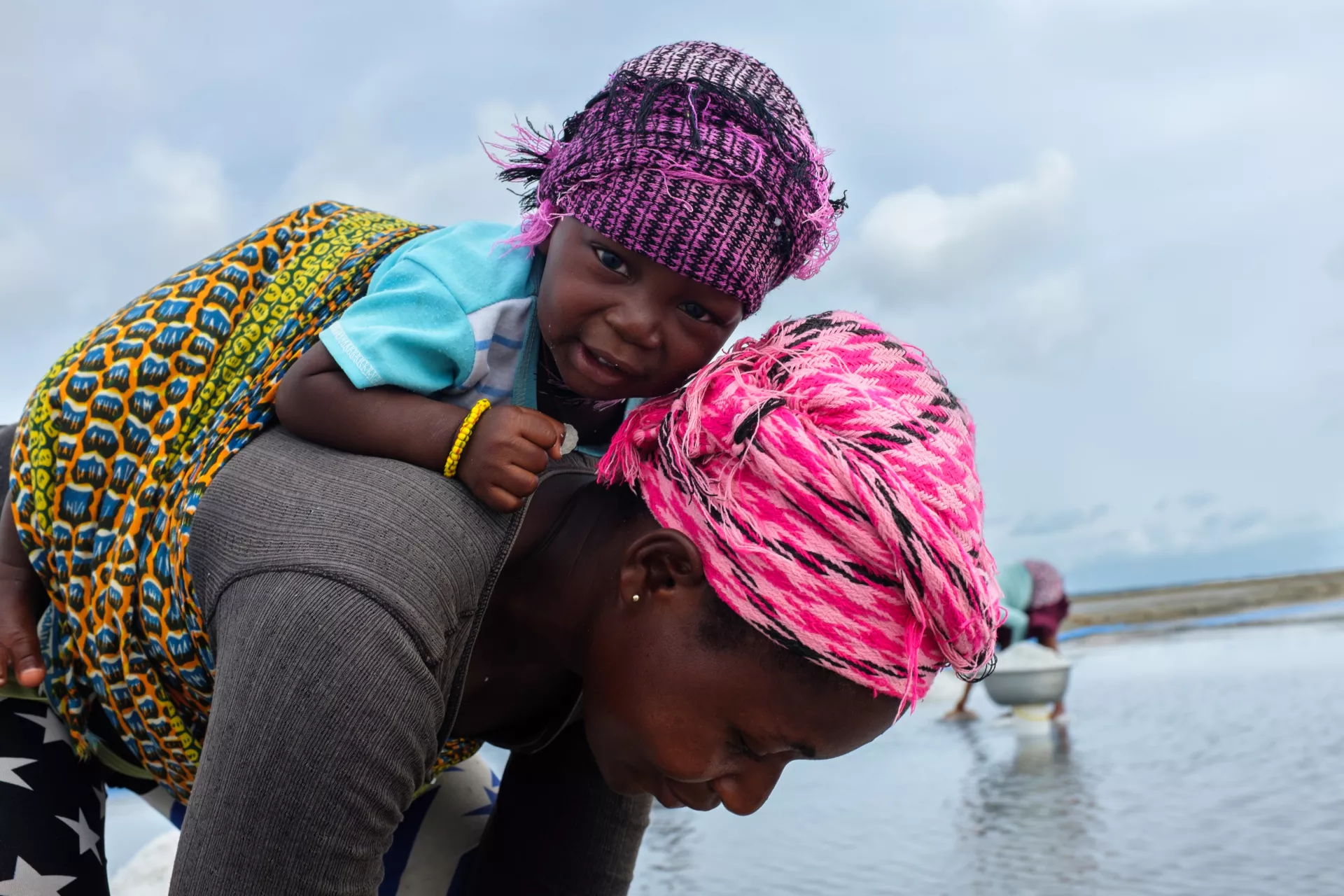Carrying her young son, Derek, on her back, Joyce gathers salt in a concentrator pan at a production operation near Koluedor on the edge of the Songhor Lagoon in Ghana on 18 May 2015.