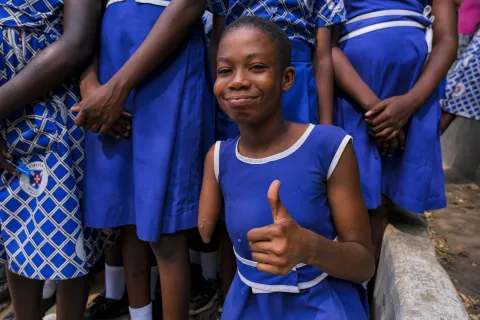 A school child smiling with a thumbs up