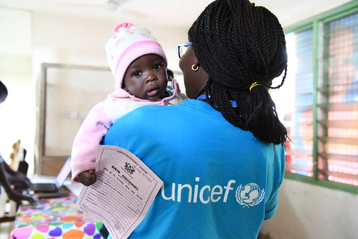 UNICEF Child Protection Officer, Ruby Anang, holds 2-month old baby Bashiru as he receives his birth certificate