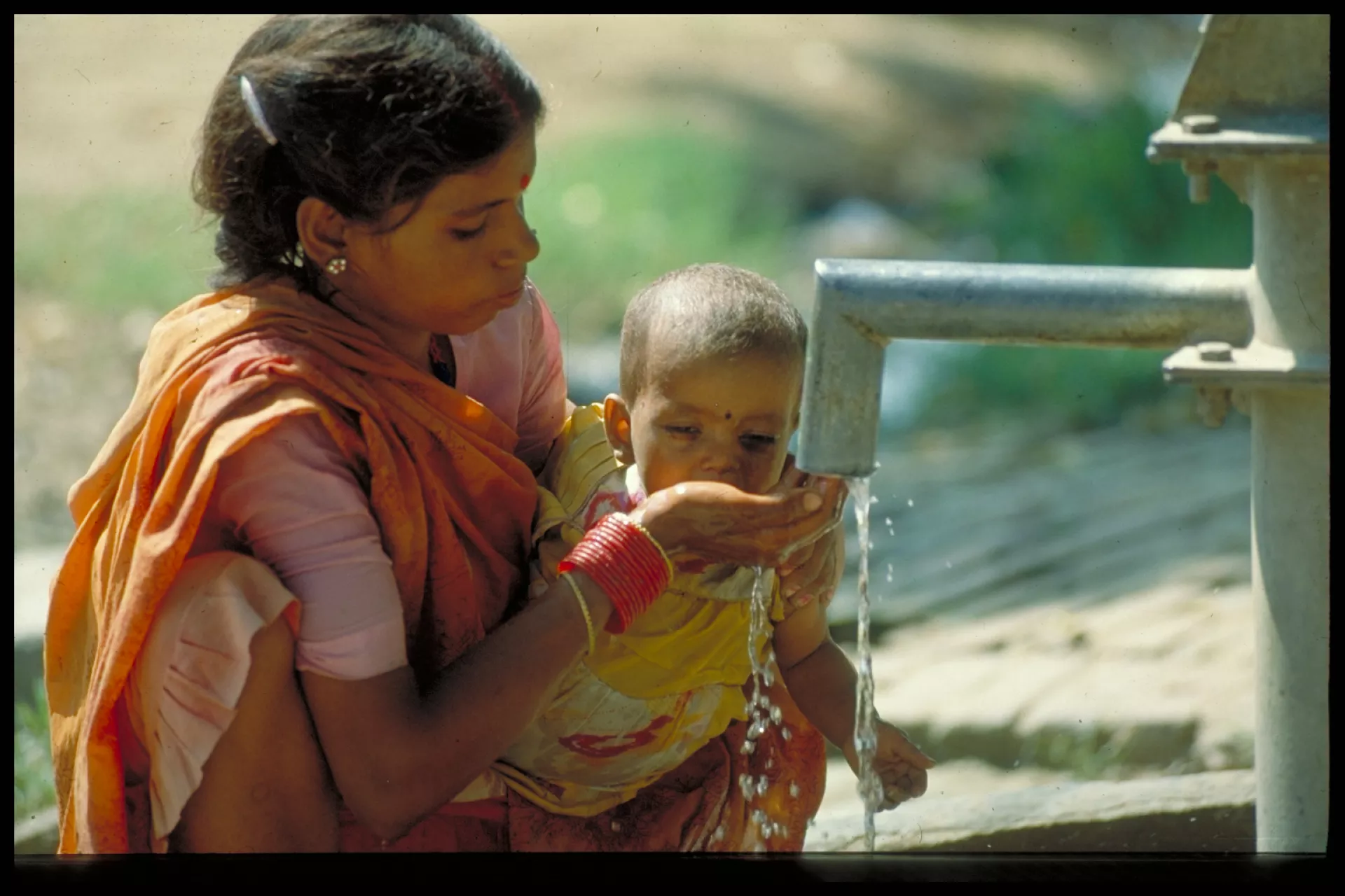 A mother giving her baby water from a water pipe.