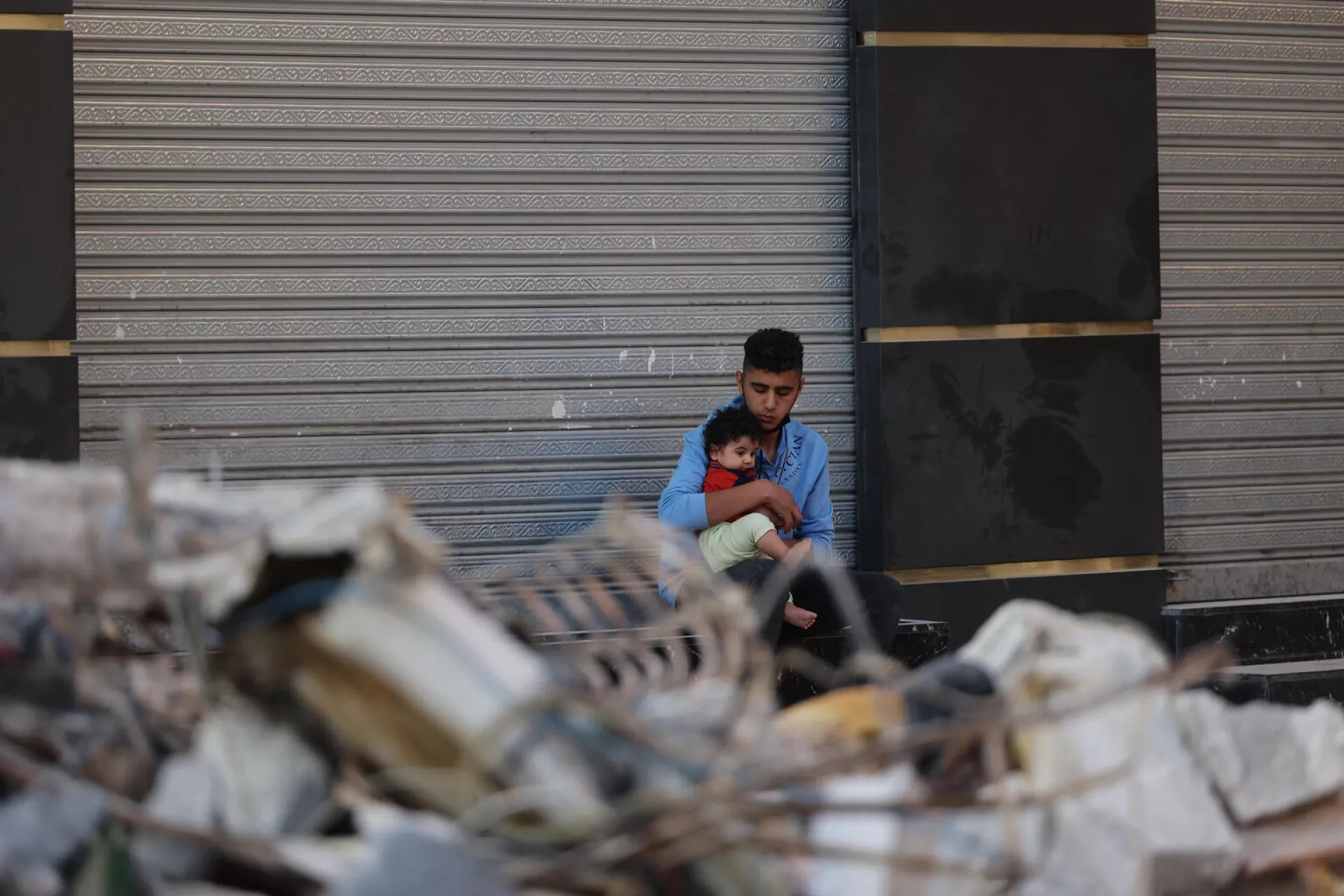 On 16 May 2021, a Palestinian man holds his son as he sits outside a closed shop in front of his destroyed home in his neighbourhood in Gaza City.