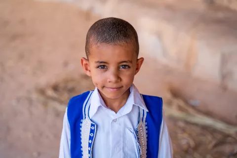 A portrait of a smiling boy in a blue vest
