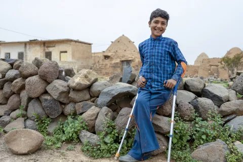 Young boy with crutches leaning against stone wall