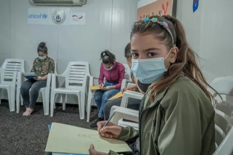 Girl looks at the camera while sitting in a classroom and wearing a mask 
