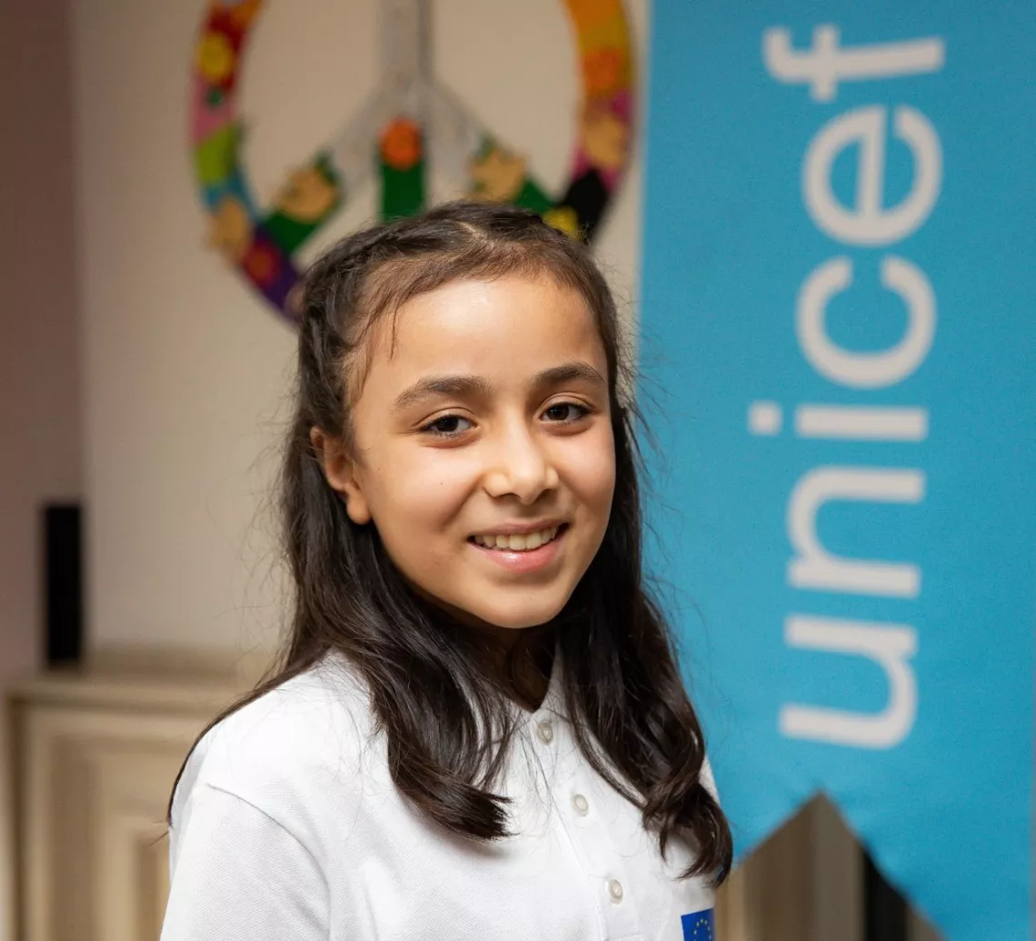 A girl smiling to the camera in front of UNICEF banner