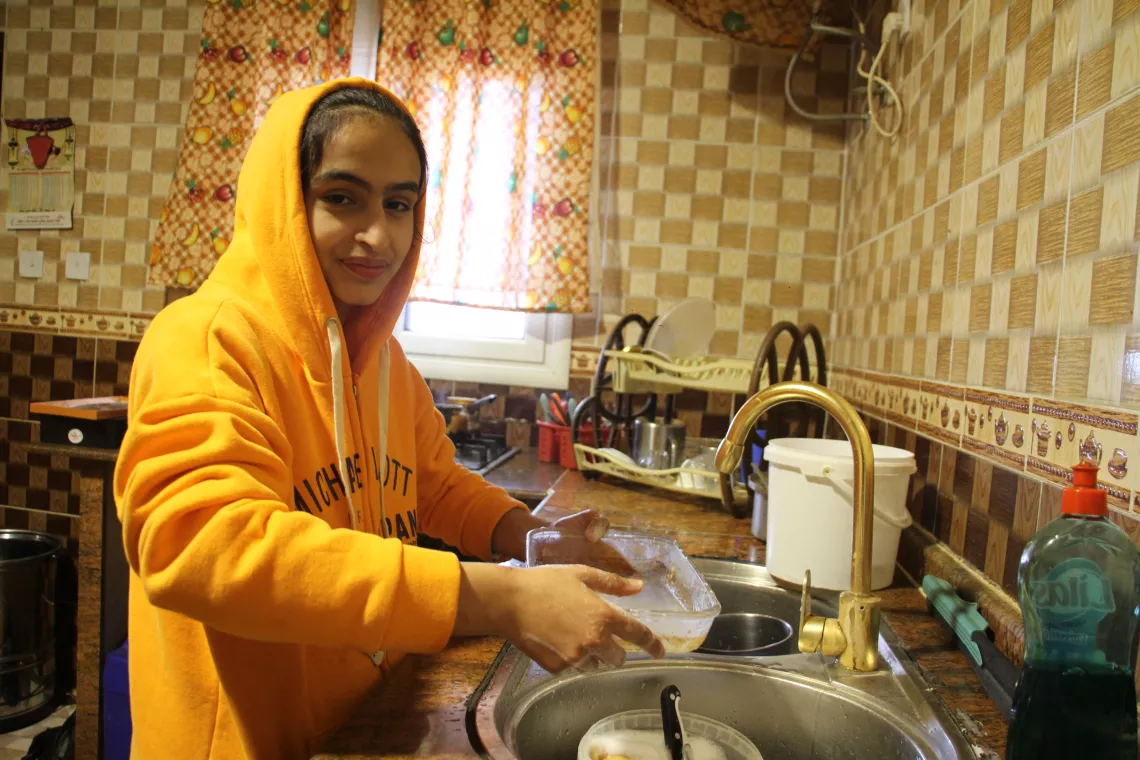 Ahlam (14), Mohamed’s daughter, with a smile as bright as her yellow hoodie, washes dishes using safe water, after UNICEF rehabilitated the bore