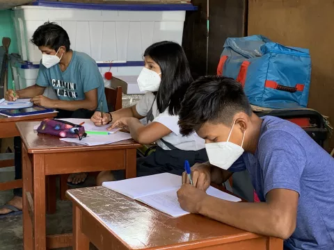 Tres adolescentes, usando mascarillas, en un salón de clases