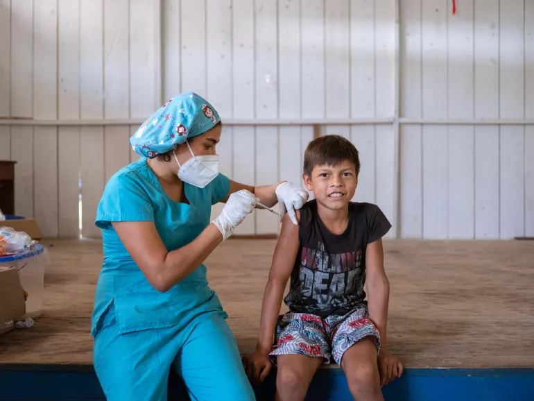 Una enfermera vacuna a un niño mientras sonríe. Ambos están sentados