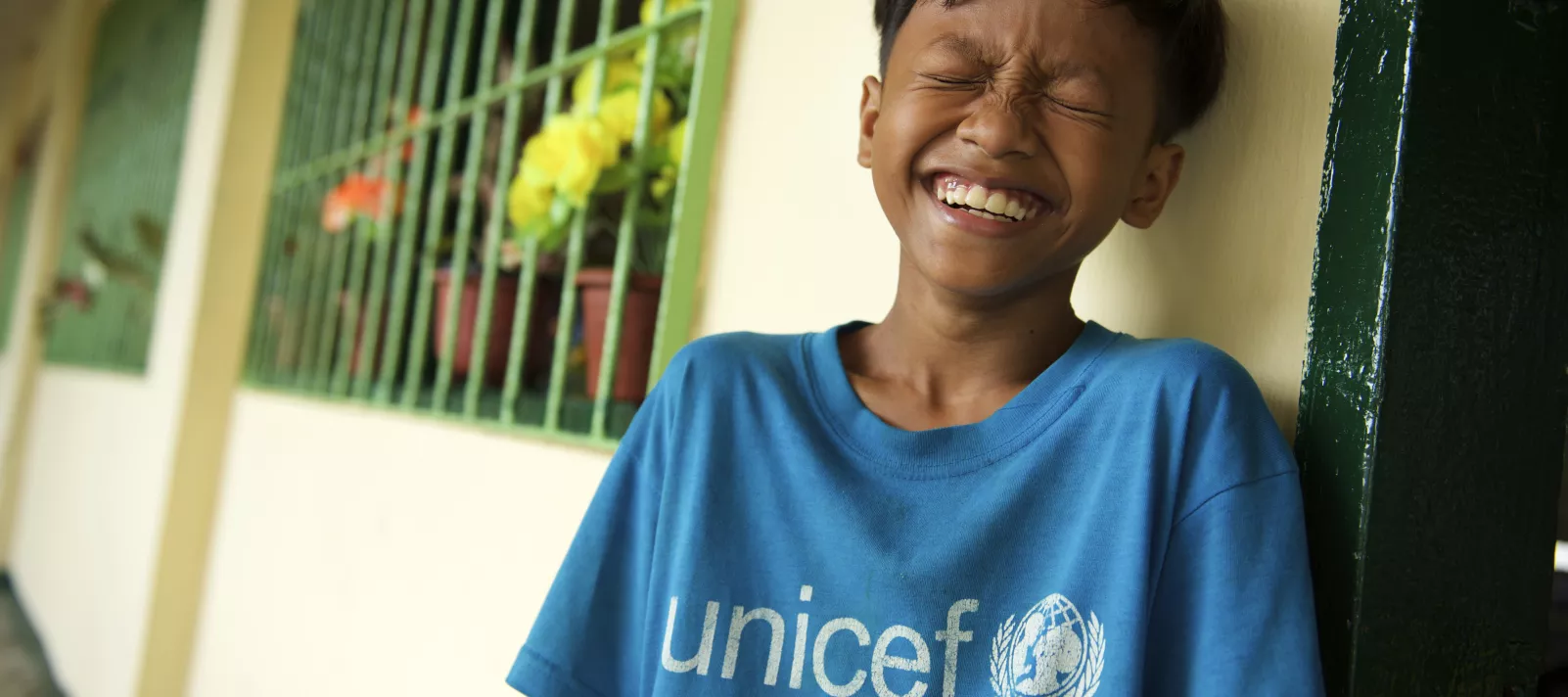 A boy in a blue UNICEF shirt smiling towards the camera with his eyes closed