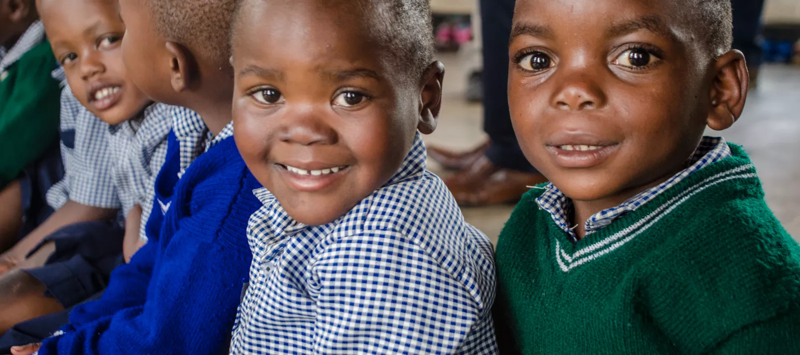 Three young children smile together in a pre-primary school